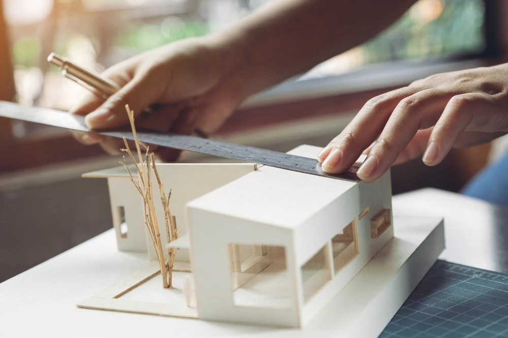 Maquettes architecturales d'immeubles résidentiels posées sur bureau avec ordinateur portable en arrière-plan flou