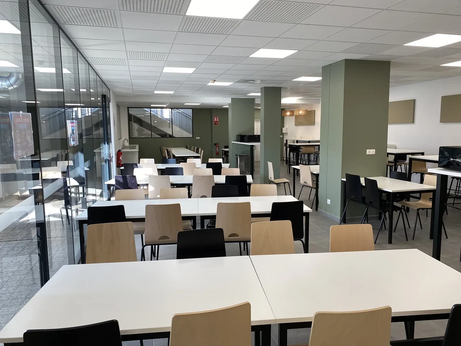 Espace de restauration d'entreprise moderne avec tables blanches rectangulaires et chaises en bois clair et noir