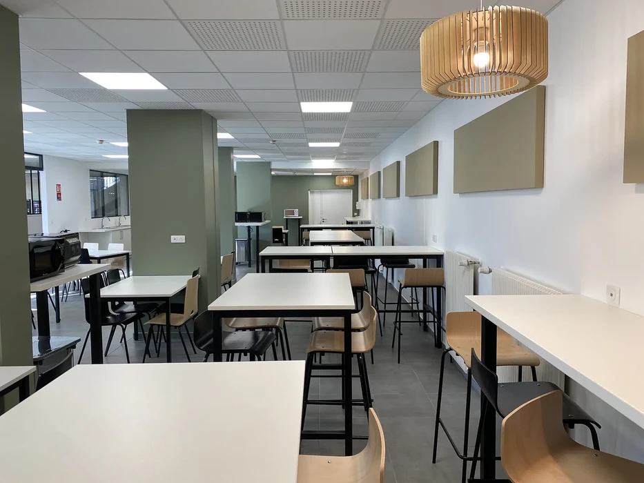 Espace de restauration d'entreprise moderne avec tables et chaises en bois clair, cuisine ouverte équipée d'électroménager professionnel